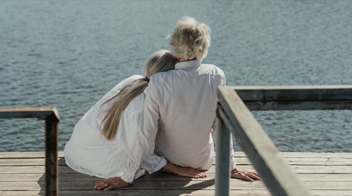 A couple sitting together at the end of a dock, looking out at the water