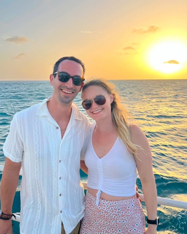 A couple on a boat deck at sunset, the sun low over open water behind them